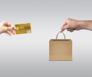 imagen de dos ordenadores desde los que sale de uno una mano con una tarjeta de credito y del otro otra mano con una bolsa