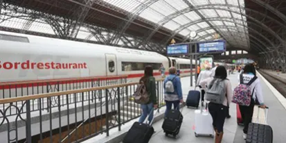 fotografía de una estación de tren con varias pasajeras en el andén llevando maletas