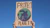Manos sosteniendo letrero con un dibujo del globo terráqueo y el lema 'Protect our planet'